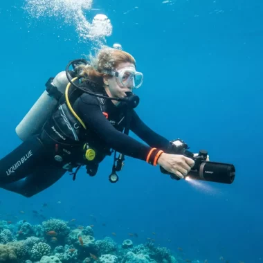 Eine Taucherin im Liquid Blue Bali Wetsuit gleitet mit einem Unterwasserscooter (DPV) über ein Korallenriff in Amed.